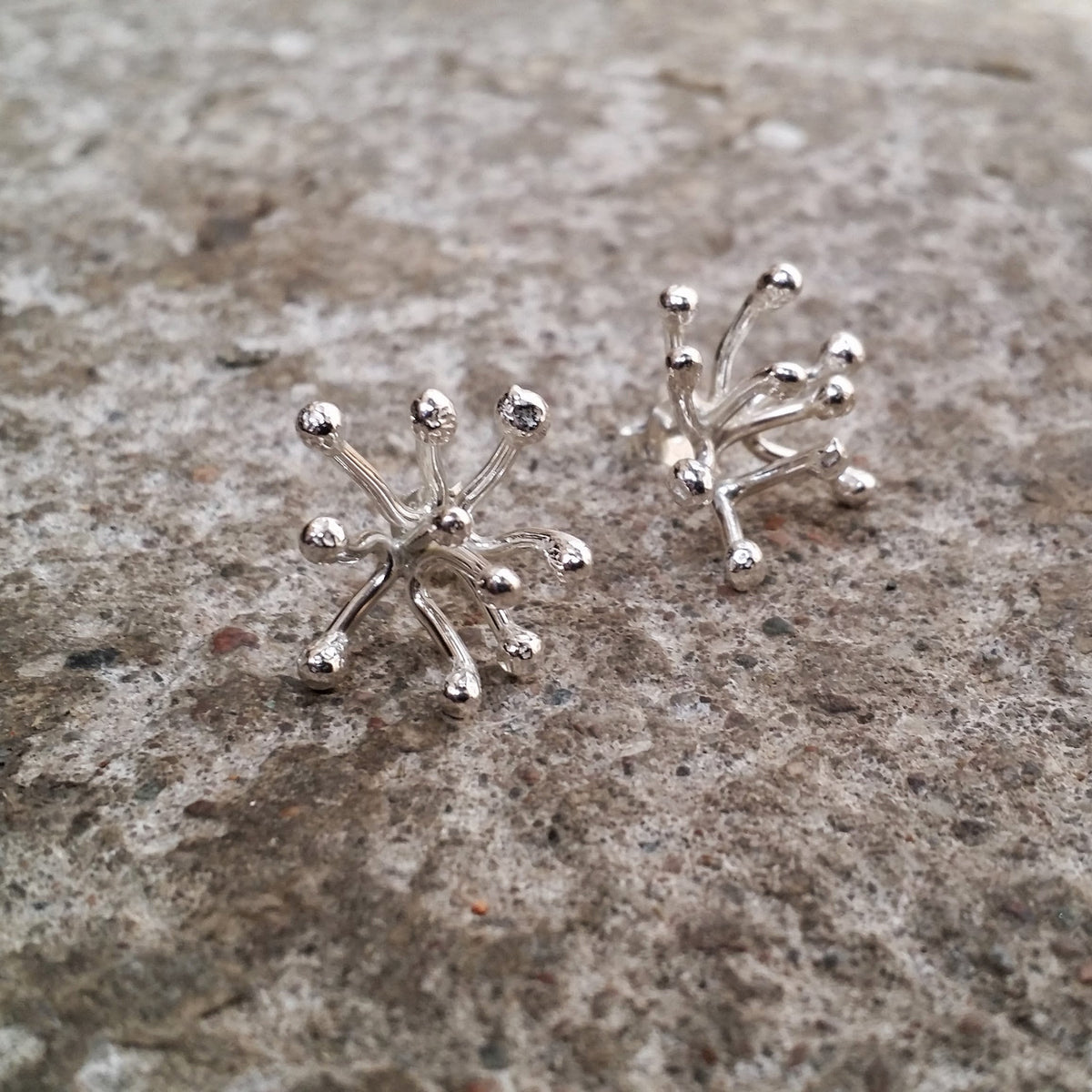 Novemberblommans handsmidda stiftörhängen i silver – ett par på stenbakgrund