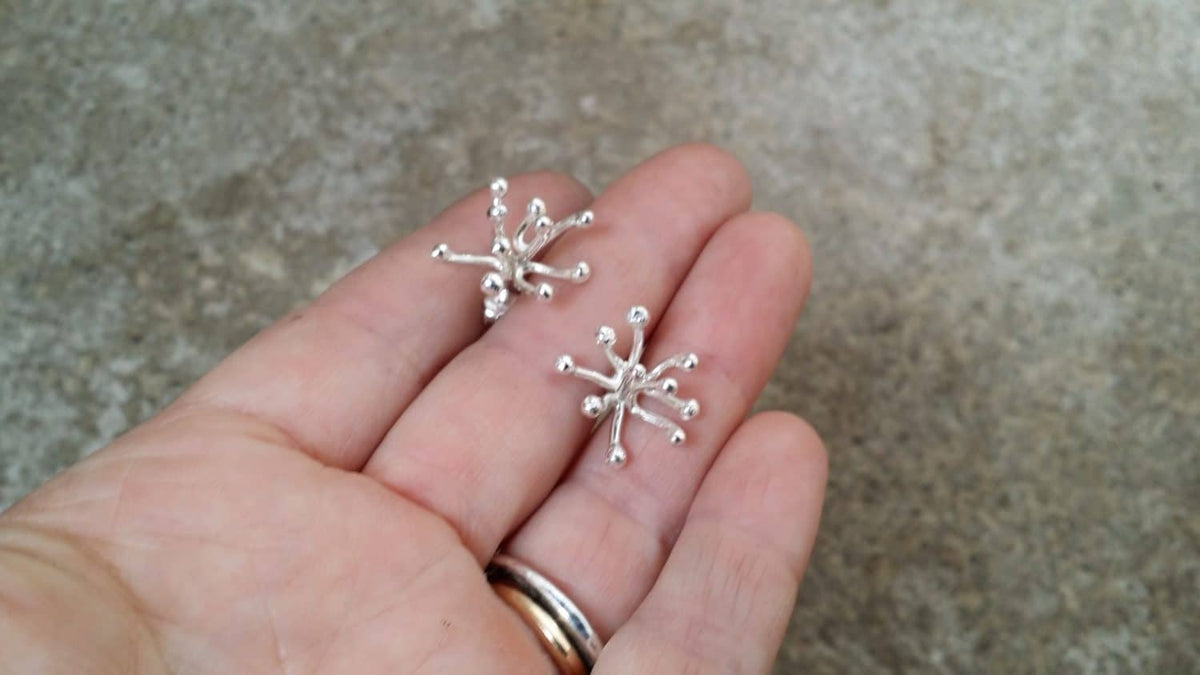 Novemberblommans stiftörhängen i silver visade i handen