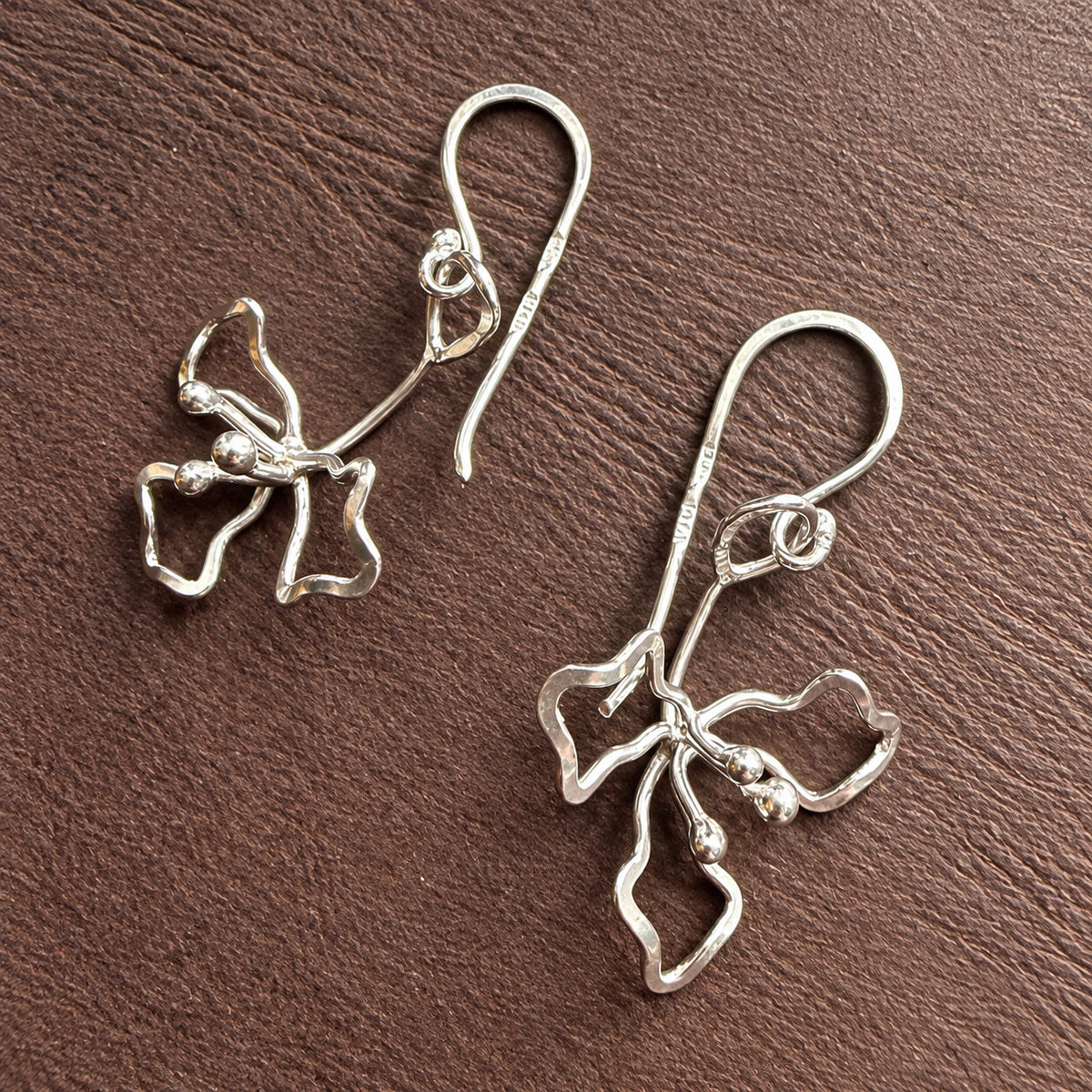 Detaljbild av oktoberblommans hängande silverörhängen med handsmidda blomformer och örkrokar