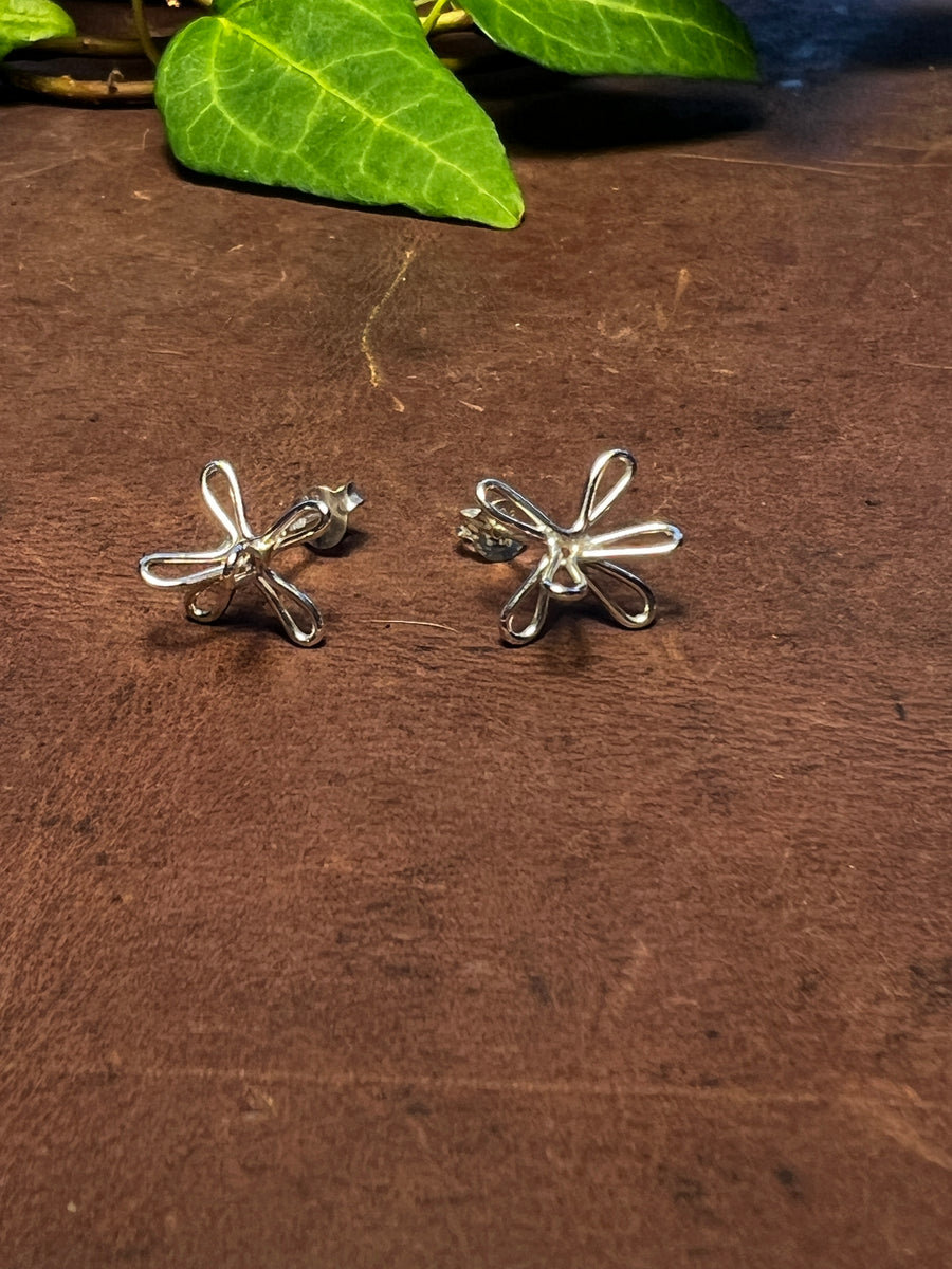 Ett par Marsblomman-stiftörhängen i silver på mörk arbetsyta med murgröna