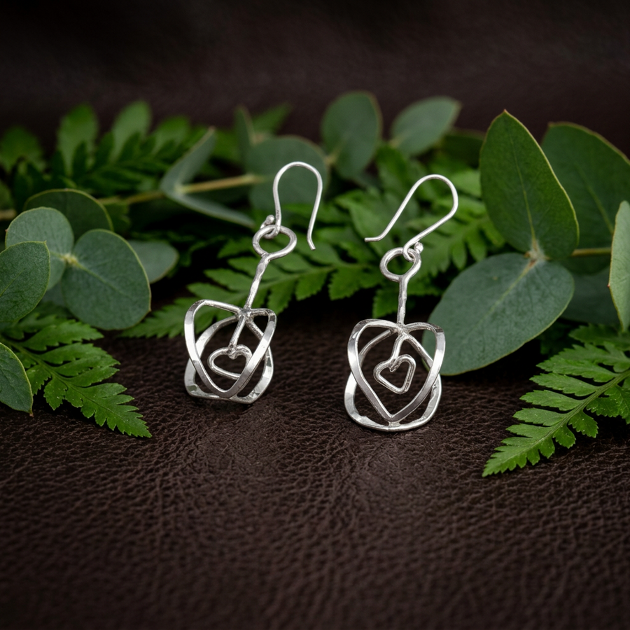 Ett par hängande Decemberblomman-örhängen i silver bland gröna blad