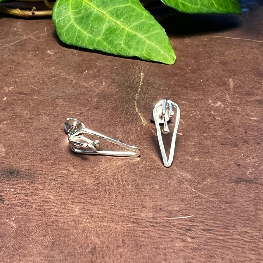 Februariblommans stiftörhängen i silver sedda från sidan på mörk arbetsyta